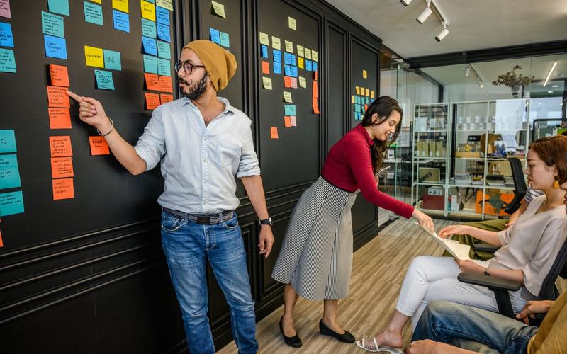Een team bespreekt de planning aan een donkere wand vol post-its.